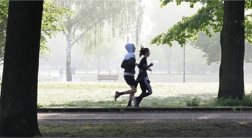 Zdjęcie przedstawia parę biegnącą w parku w słoneczny dzień