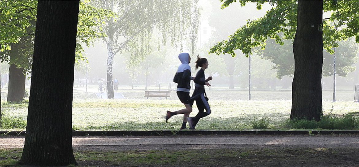 Zdjęcie przedstawia parę biegnącą w parku w słoneczny dzień