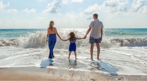 Zdjęcie przedstawia rodzinę stojącą na brzegu plaży