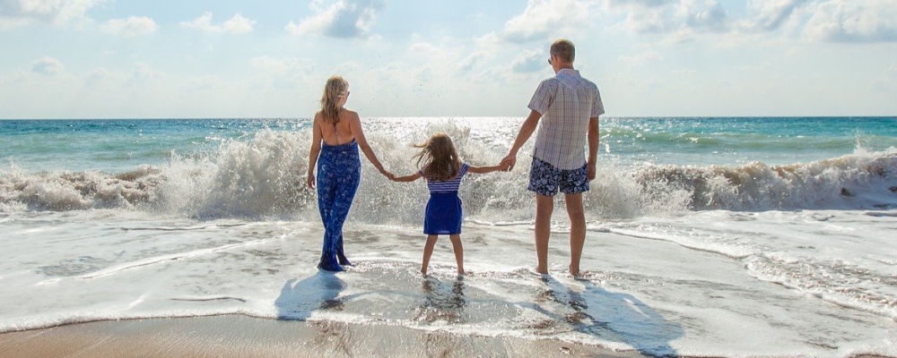 Zdjęcie przedstawia rodzinę stojącą na brzegu plaży